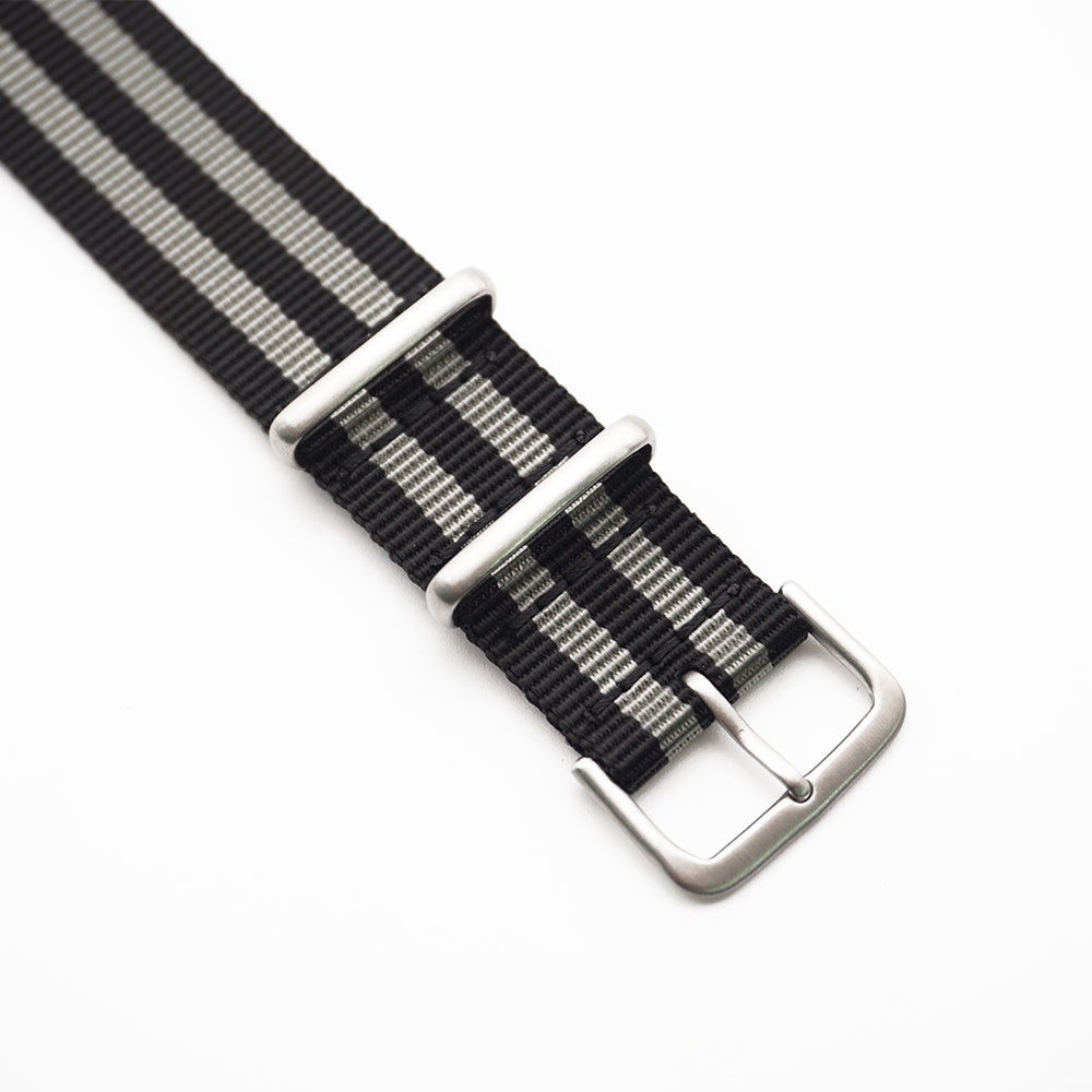 Spännet på ett grå- och svartrandigt natoband.